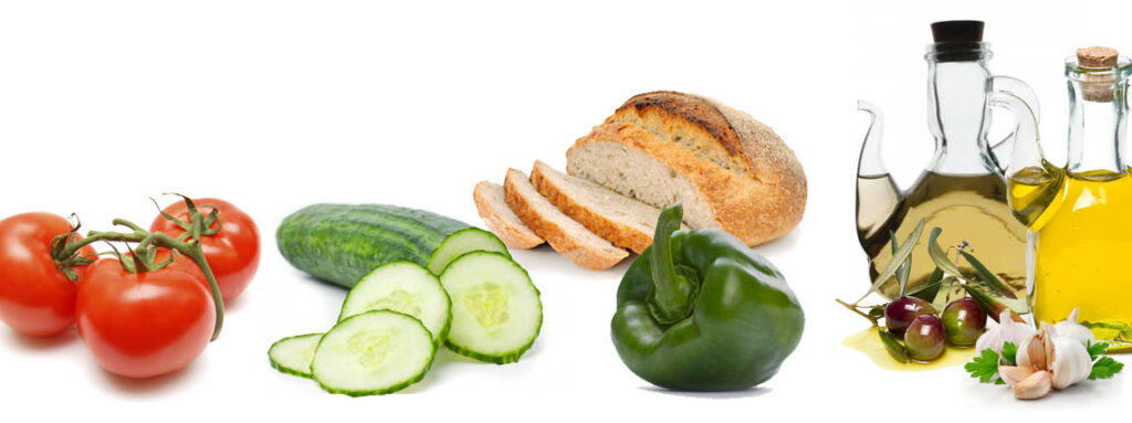 Ingredientes frescos para gazpacho andaluz: pan rústico parcialmente cortado, pepino en rodajas y pimiento verde brillante sobre fondo blanco. Preparación saludable y tradicional de la cocina mediterránea.